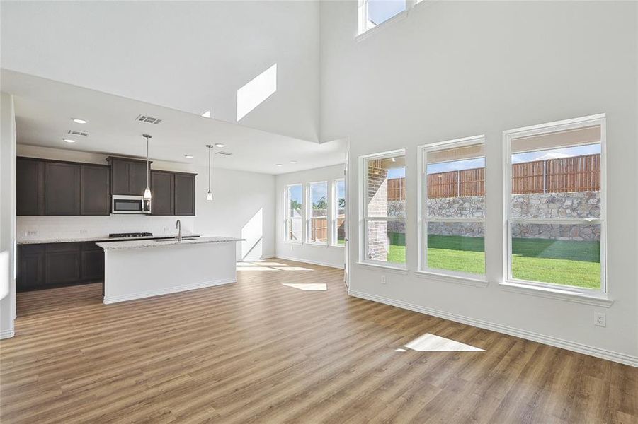 Unfurnished living room featuring a healthy amount of sunlight, sink, light hardwood / wood-style floors, and a high ceiling