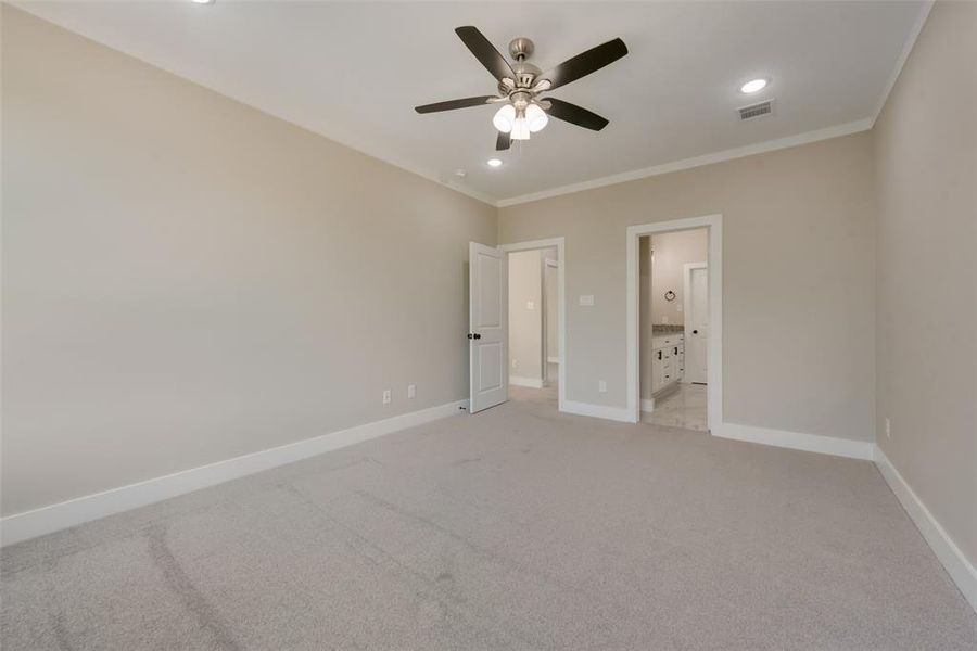 Unfurnished bedroom with ceiling fan, light colored carpet, ensuite bath, and ornamental molding