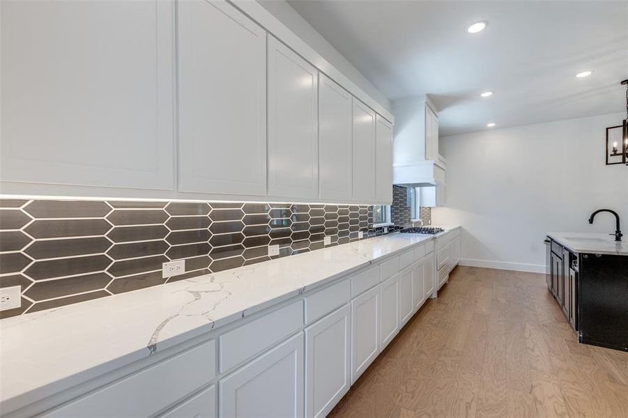 Kitchen with sink, tasteful backsplash, light hardwood / wood-style flooring, white cabinetry, and light stone countertops