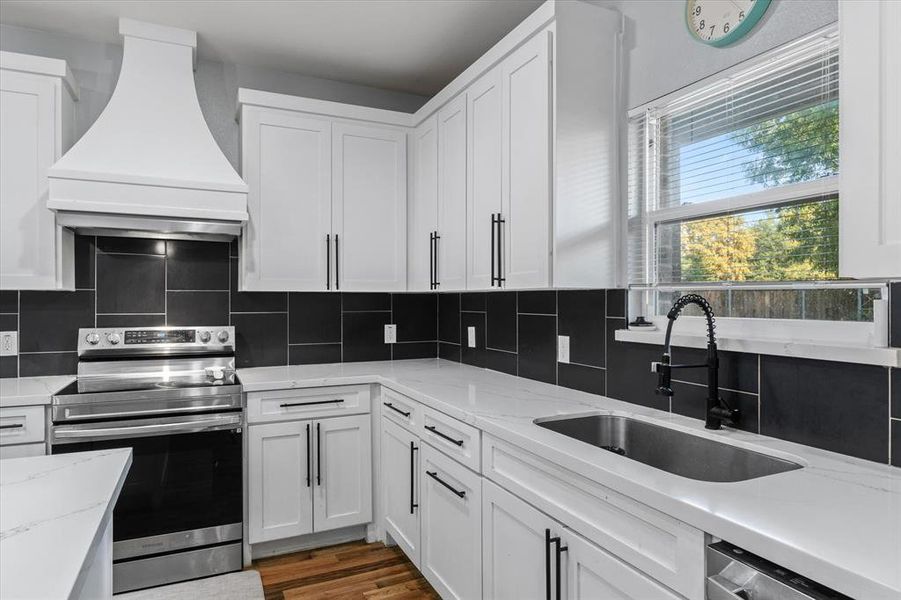 Kitchen featuring custom range hood, white cabinetry, sink, and stainless steel appliances