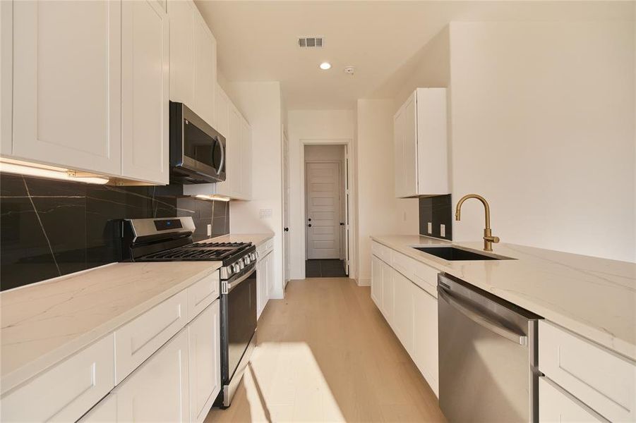 Kitchen featuring sink, white cabinets, stainless steel appliances, backsplash, and light stone countertops