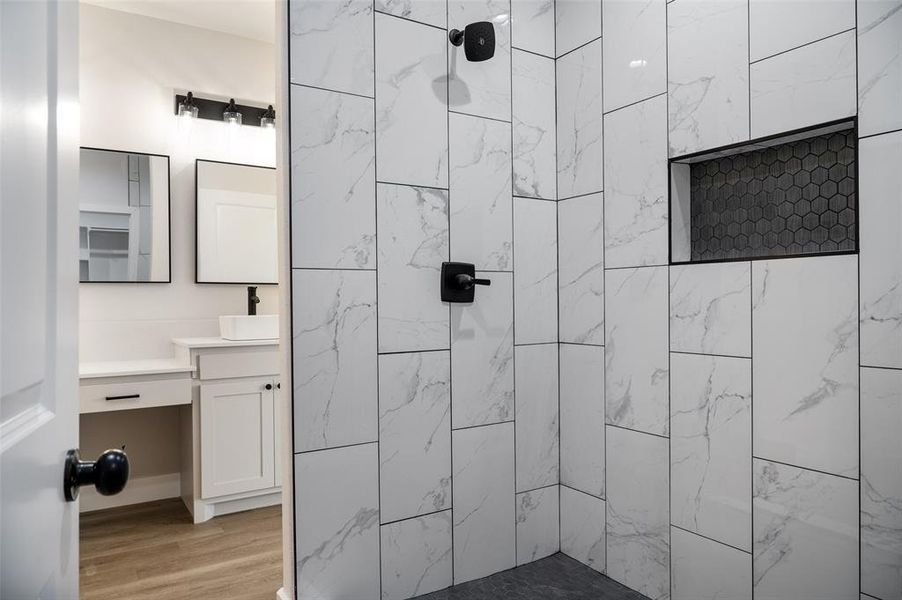 Bathroom with tiled shower, vanity, and hardwood / wood-style floors