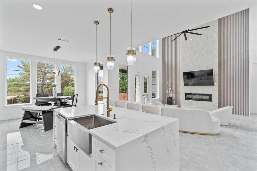 Kitchen with pendant lighting, light stone countertops, a center island with sink, white cabinetry, and a fireplace