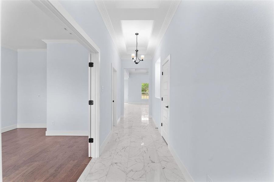 Corridor with hardwood / wood-style floors, a notable chandelier, and crown molding