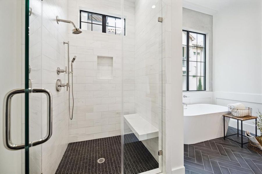 The bathroom has a walk-in shower with tile walls, frameless glass door, built-in shower niche, and stone bench seating, alongside herringbone ceramic tile flooring. A steel window offers northern exposure.
