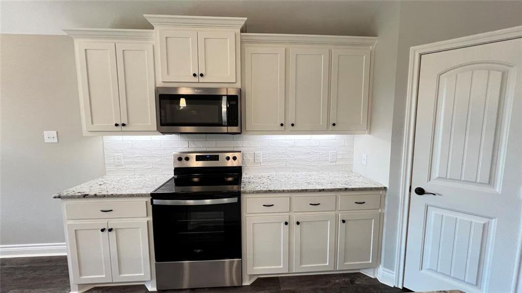 Kitchen with decorative backsplash, stainless steel appliances, white cabinets, and light stone counters