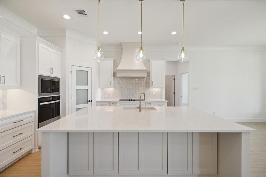 Kitchen with white cabinets, hanging light fixtures, light stone countertops, appliances with stainless steel finishes, and premium range hood