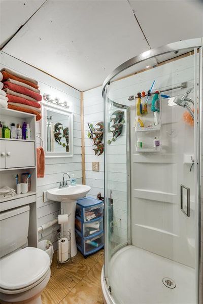 Bathroom with wooden walls, a shower with door, and toilet