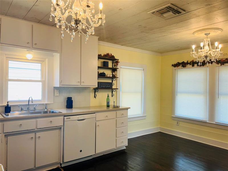 Kitchen featuring dishwasher, sink, hanging light fixtures, white cabinets, and dark wood-type flooring