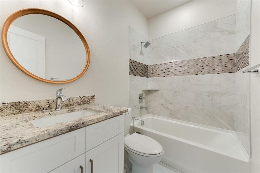 Full bathroom with tiled shower / bath combo, vanity, and toilet