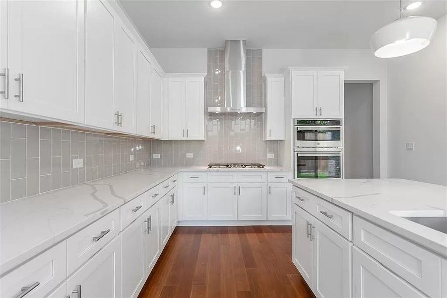 Kitchen featuring dark hardwood / wood-style flooring, decorative backsplash, stainless steel appliances, and wall chimney exhaust hood