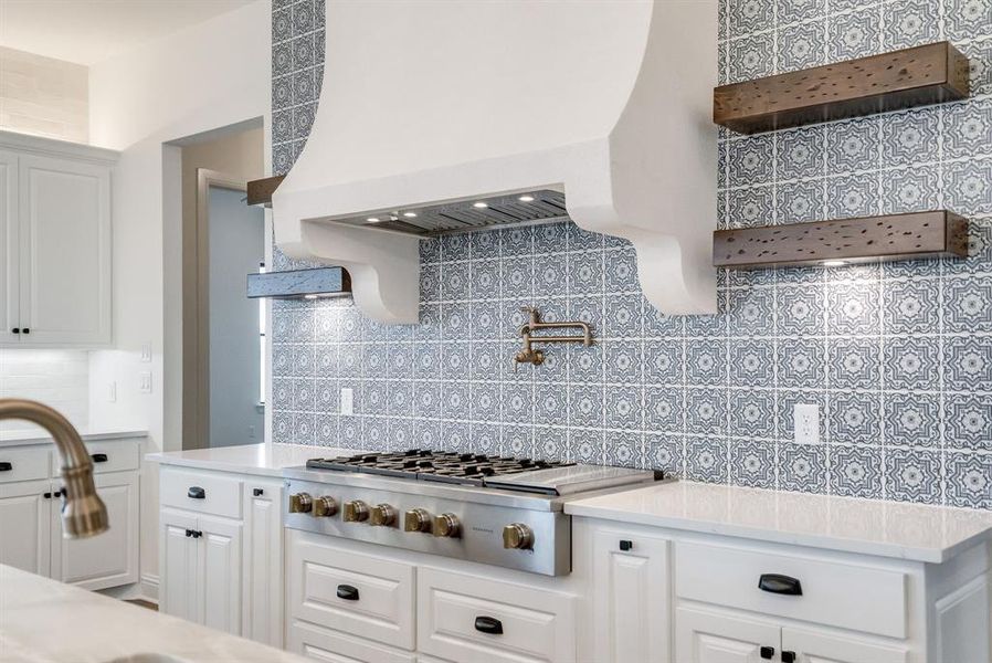 Kitchen with custom exhaust hood, backsplash, stainless steel gas cooktop, and white cabinets