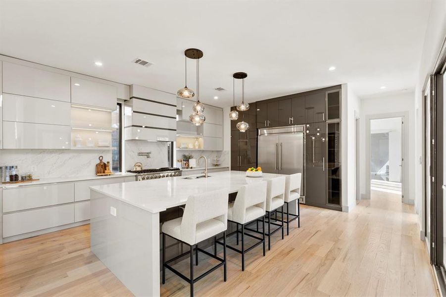 Kitchen featuring white cabinets, a kitchen island with sink, light wood-type flooring, and decorative backsplash