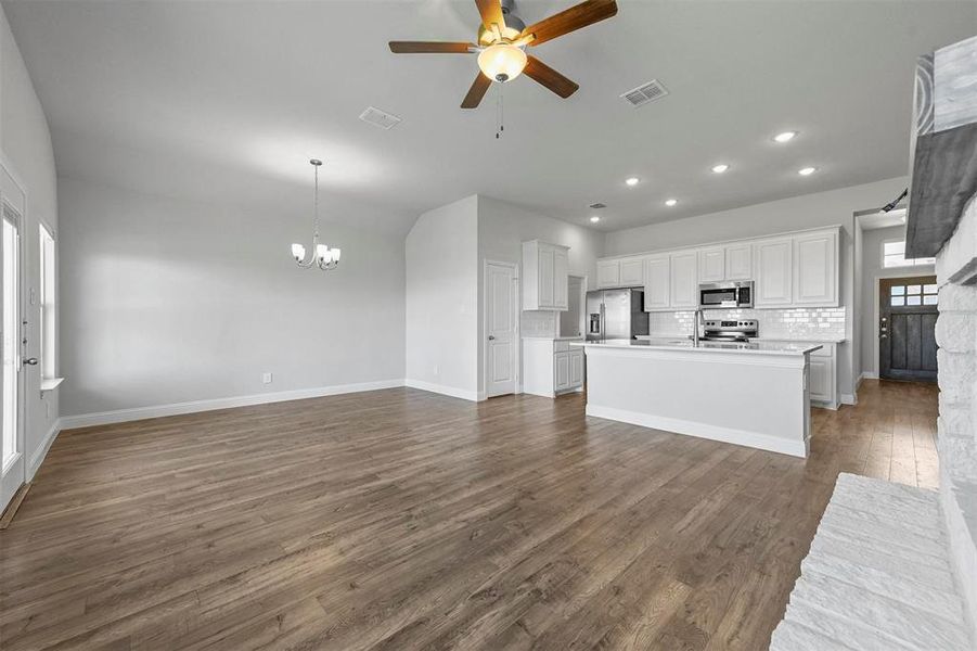 Kitchen featuring dark hardwood / wood-style flooring, ceiling fan with notable chandelier, stainless steel appliances, a kitchen island with sink, and backsplash
