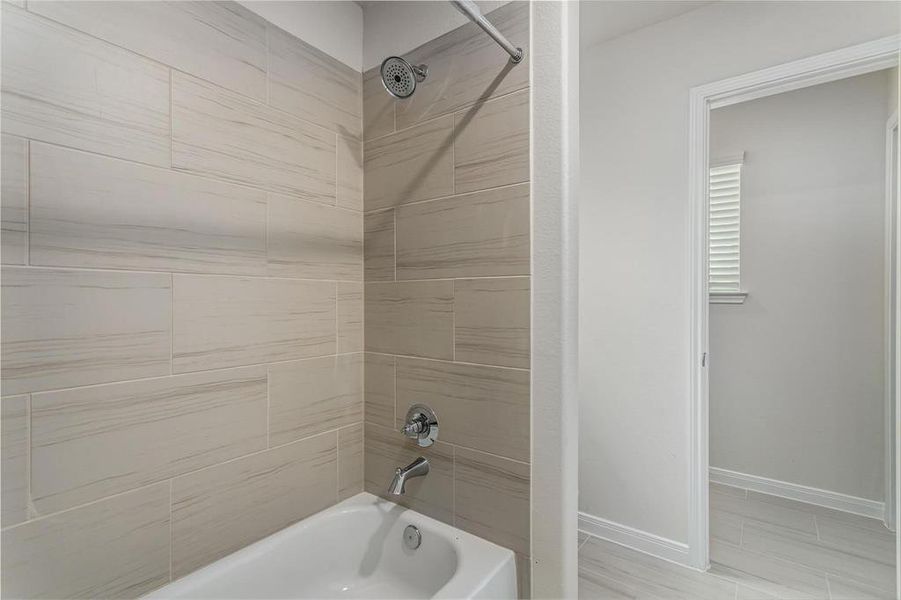 Indulge in the luxury of this beautifully tiled shower and tub combo, featuring modern fixtures and a relaxing ambiance. The neutral tile design adds a touch of elegance, while the showerhead provides a spa-like experience right at home. Photos are from another Rylan floor plan.