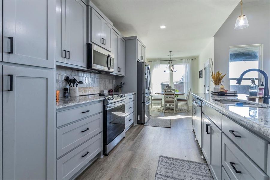 Kitchen with light hardwood / wood-style floors, sink, decorative light fixtures, and appliances with stainless steel finishes