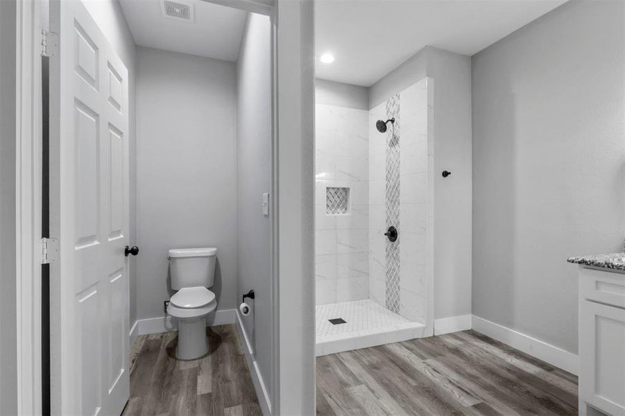 Bathroom featuring a tile shower, vanity, toilet, and hardwood / wood-style floors