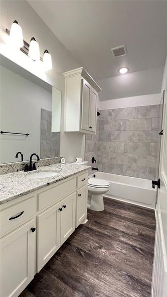 Full bathroom with hardwood / wood-style floors, tiled shower / bath combo, vanity, and toilet