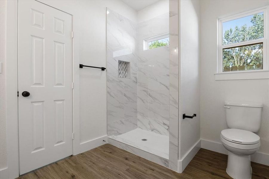 Bathroom featuring a tile shower, hardwood / wood-style floors, and toilet