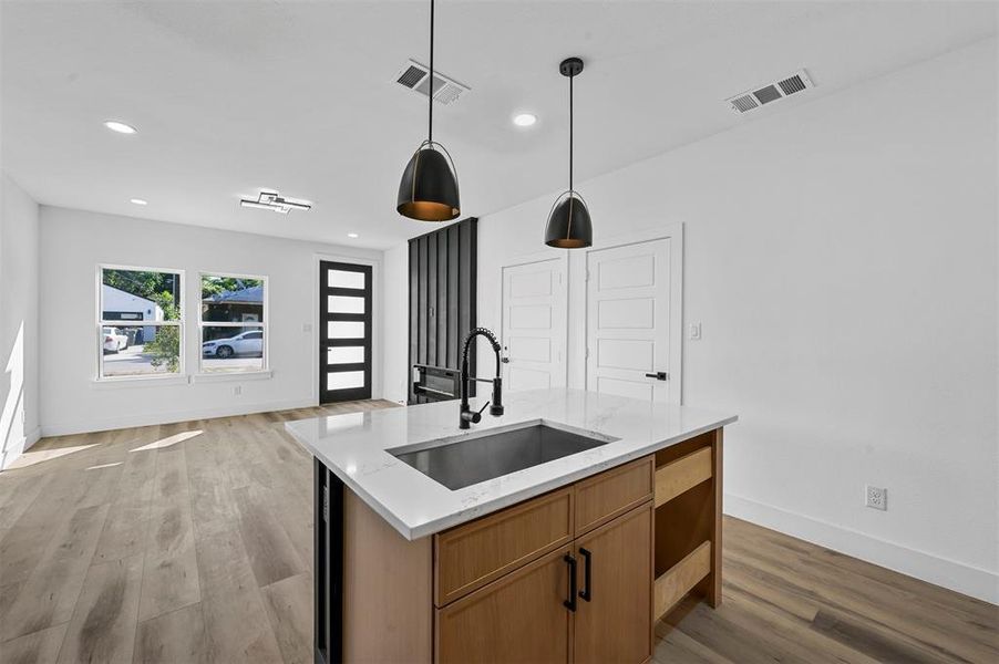 Kitchen with an island with sink, light stone counters, wood-type flooring, pendant lighting, and sink