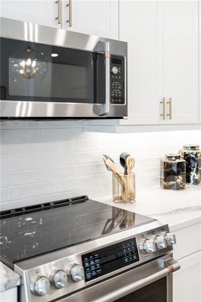 Interior details featuring 42' inch upper cabinets, appliances with stainless steel finishes, light stone counters, and tasteful backsplash