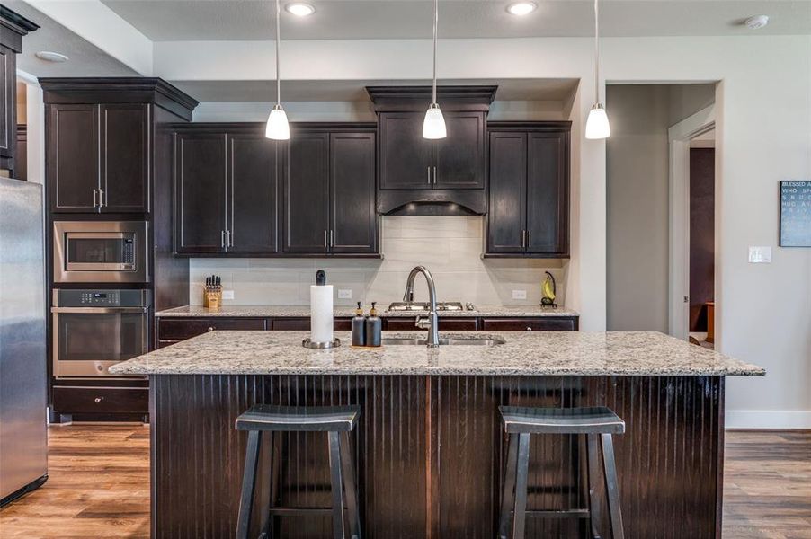 Kitchen with granite countertops, stainless steel appliances, luxury vinyl plank flooring, backsplash, and pendant lighting over spacious island