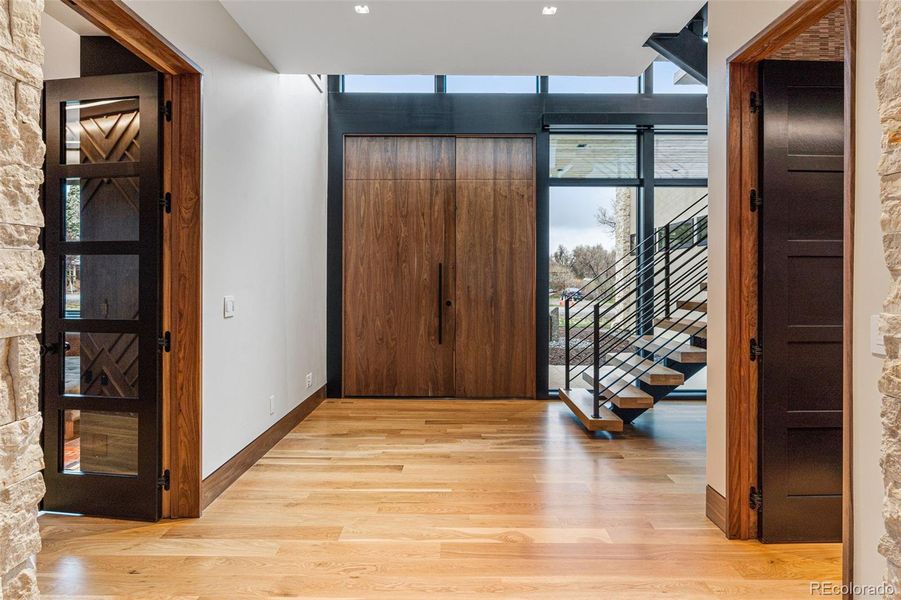 A grand entry with custom solid walnut pivot door (with Emtek hardware). The door to the right is a walk-in entry closet with built-in Shiloh Cabinets, a Pental Quartz slab bench and Black Edition Wallpaper.