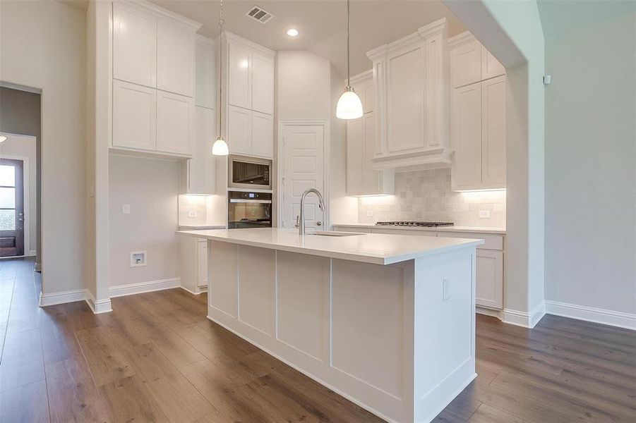 Kitchen featuring backsplash, a kitchen island with sink, hardwood / wood-style floors, appliances with stainless steel finishes, and sink