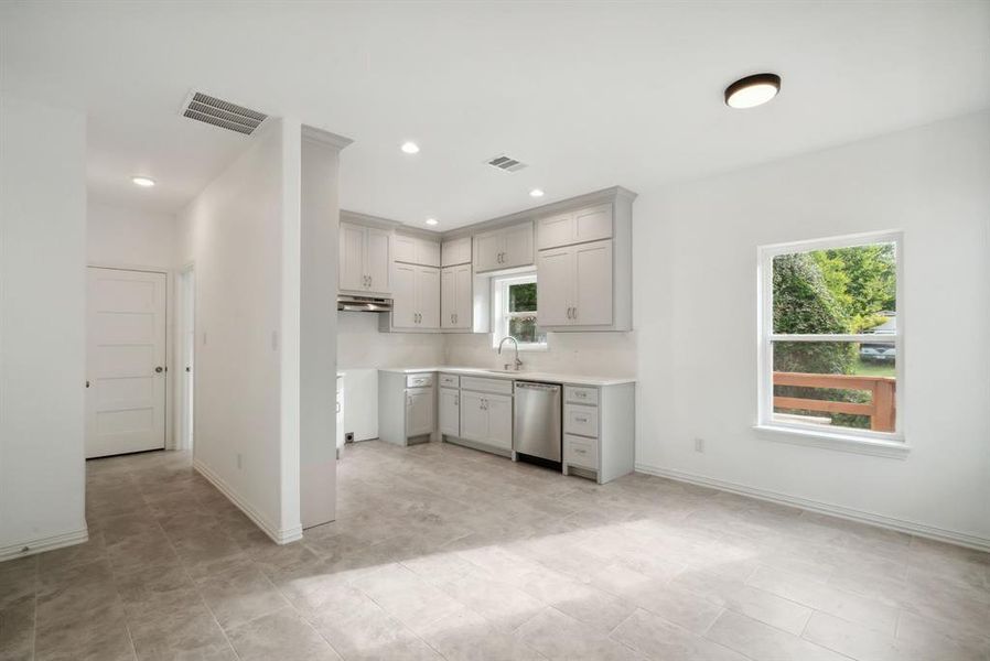 Kitchen featuring light tile patterned flooring, gray cabinets, sink, and stainless steel dishwasher