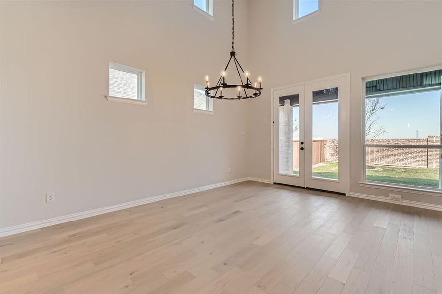 Spare room with a high ceiling, light hardwood / wood-style flooring, and an inviting chandelier