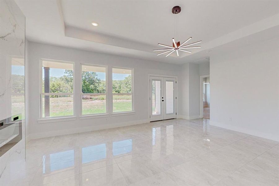 Unfurnished room with a raised ceiling, an inviting chandelier, light tile patterned floors, and french doors