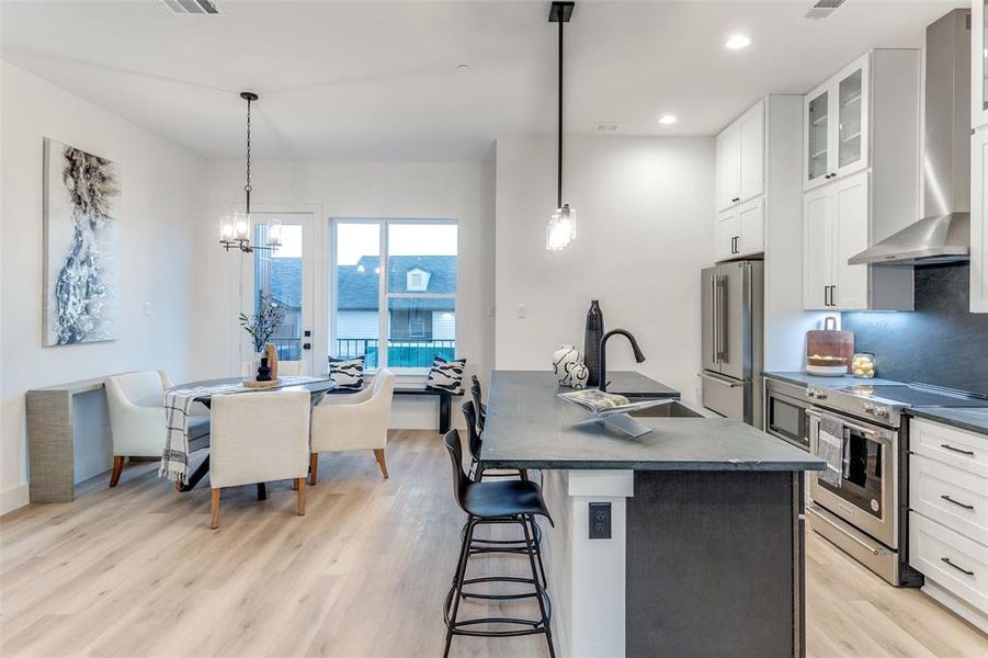 Kitchen featuring appliances with stainless steel finishes, white cabinetry, an island with sink, and decorative light fixtures