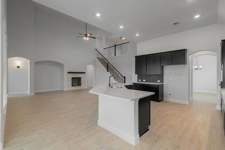 Kitchen with a tiled fireplace, light stone countertops, light hardwood / wood-style floors, ceiling fan, and high vaulted ceiling