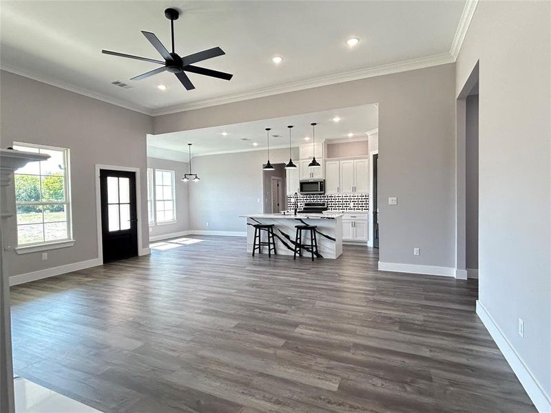 Unfurnished living room featuring ceiling fan, ornamental molding, sink, and dark wood-type flooring