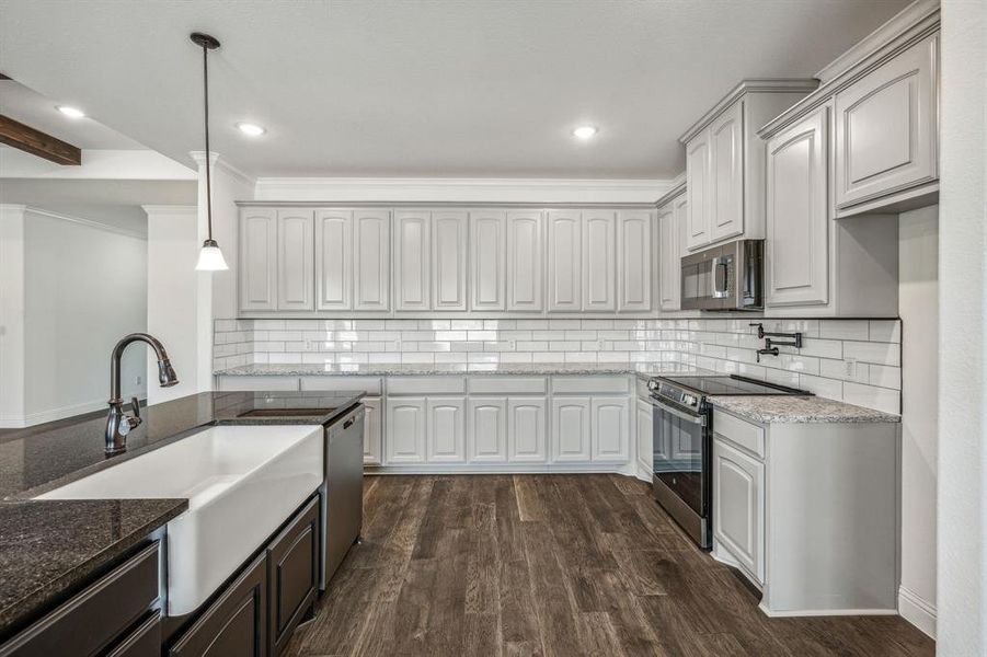 Kitchen with ornamental molding, appliances with stainless steel finishes, dark hardwood / wood-style flooring, and decorative backsplash