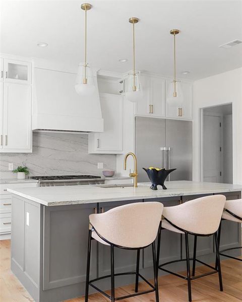 Kitchen with pendant lighting, an island with sink, white cabinets, light hardwood / wood-style flooring, and appliances with stainless steel finishes