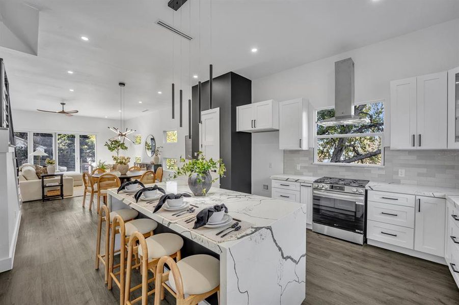 Kitchen with stainless steel gas range oven, white cabinets, decorative light fixtures, and island exhaust hood