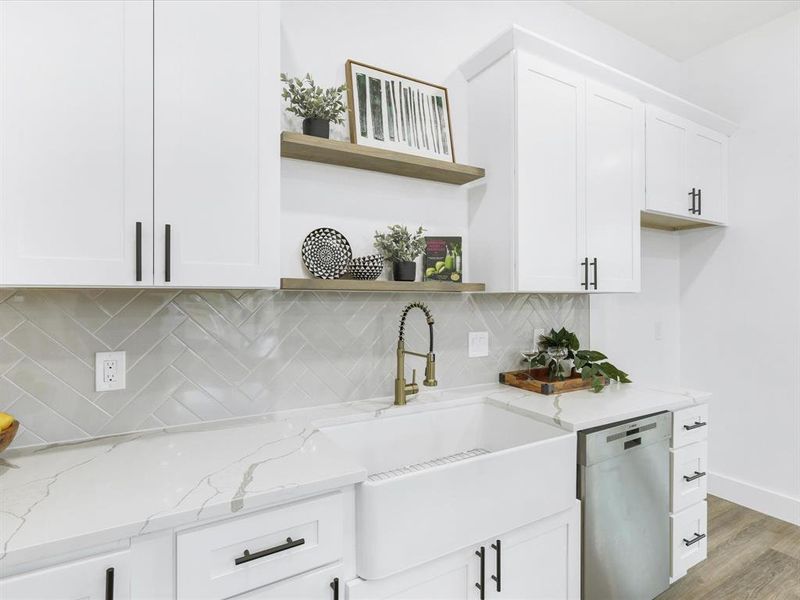 Kitchen with light hardwood / wood-style flooring, white cabinets, light stone counters, decorative backsplash, and dishwasher