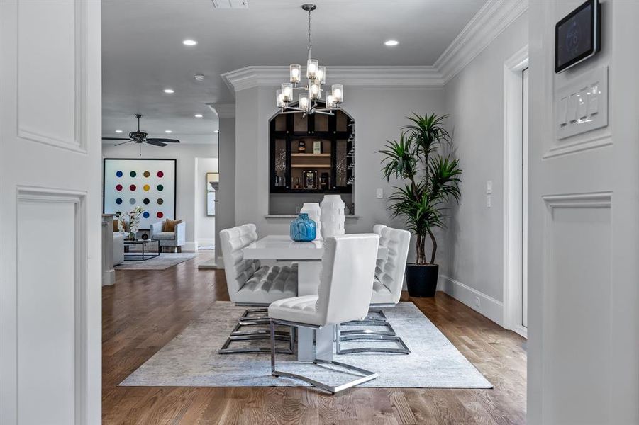 Dining space with wood-type flooring, ceiling fan with notable chandelier, and crown molding