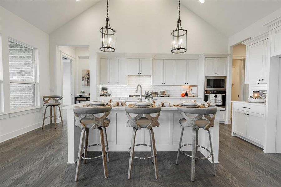 Kitchen with white cabinetry, hanging light fixtures, and a kitchen island with sink