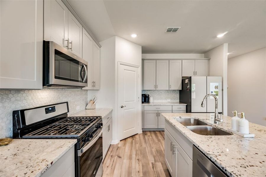 Kitchen featuring light hardwood / wood-style floors, light stone countertops, stainless steel appliances, backsplash, and sink