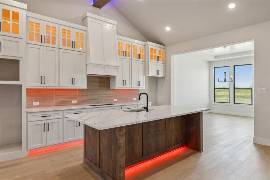 Kitchen with a center island with sink, sink, decorative backsplash, white cabinets, and vaulted ceiling with beams