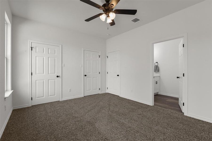 Unfurnished bedroom featuring dark colored carpet, multiple closets, ensuite bath, and ceiling fan