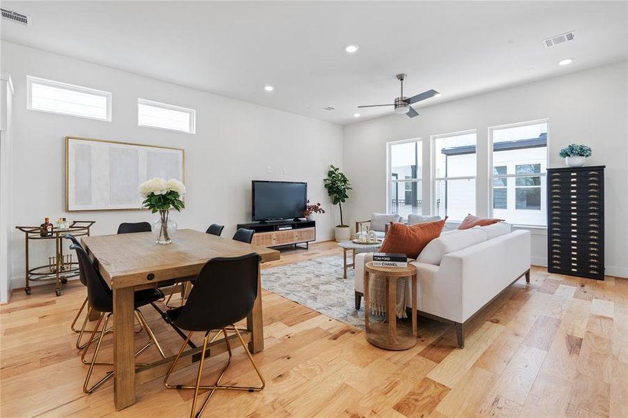 The elevated dining area boasts a commanding vantage point overlooking the sun-drenched living room, where three large windows illuminate the space with natural light and create an airy ambiance.