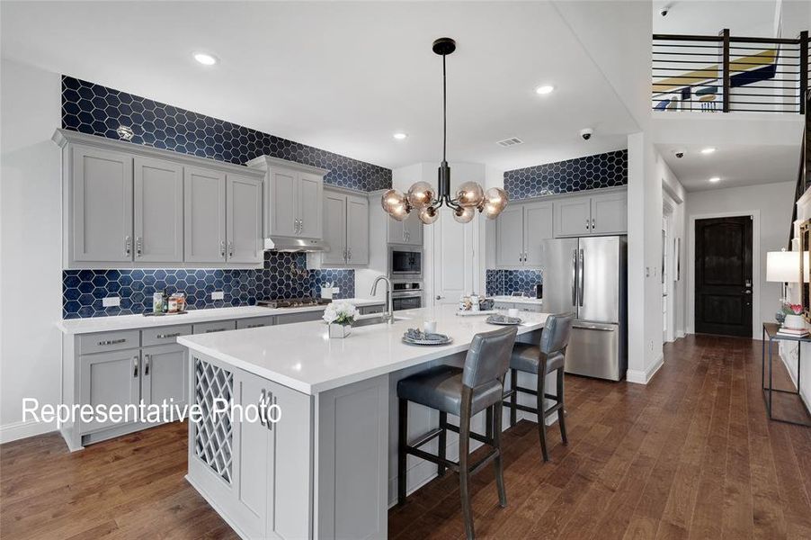 Kitchen with tasteful backsplash, an island with sink, decorative light fixtures, dark hardwood / wood-style flooring, and appliances with stainless steel finishes