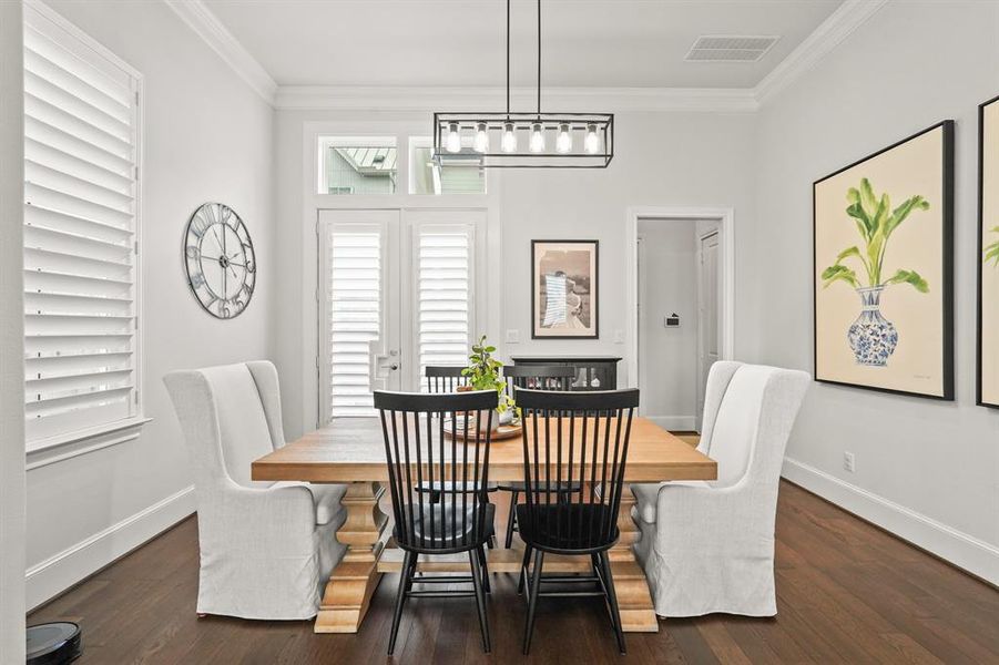 Spacious dining room with engineered wood floors, pendant lighting, plantation shutters, crown molding details, and direct access to the kitchen.