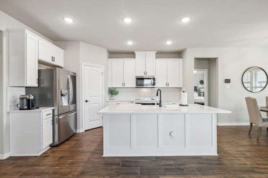 Kitchen featuring white cabinets, decorative backsplash, a center island with sink, and stainless steel appliances