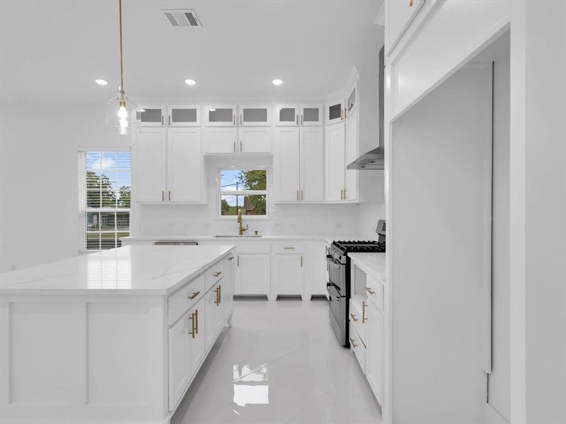 Kitchen with white cabinetry, gas range, a center island, and light stone countertops