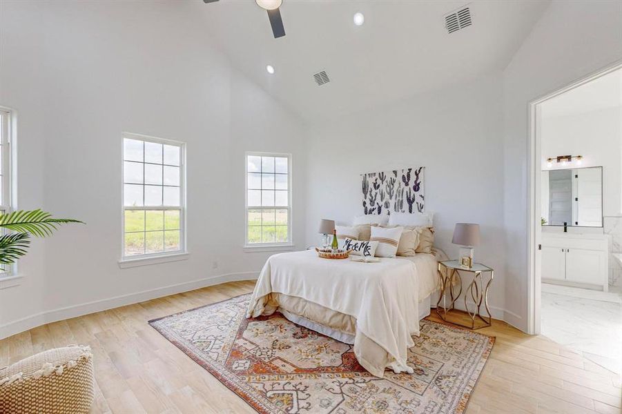 Bedroom featuring light hardwood / wood-style flooring, ensuite bath, ceiling fan, and high vaulted ceiling