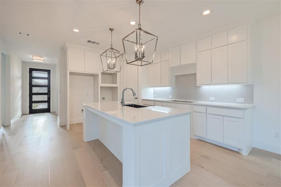 Kitchen with light hardwood / wood-style floors, an island with sink, white cabinets, an inviting chandelier, and decorative light fixtures